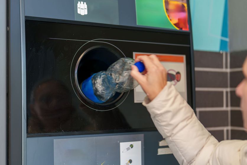 Person recycling a plastic bottle at a modern recycling station inside a city environment Débat sur la consigne des bouteilles en plastique