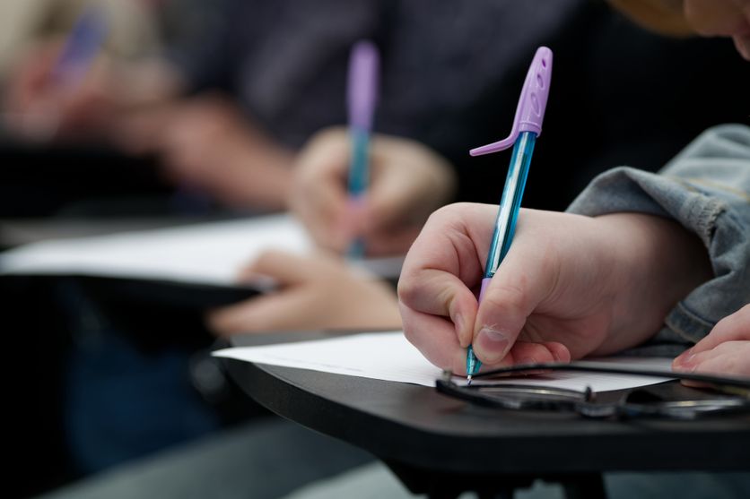 Group of students taking a test at their desks. Selective focus on a hand holding a pen over a blank sheet. Ideal for university lectures, homework, and diligence themes. Photo Le questionnaire sur les violences sexistes et sexuelles en débat